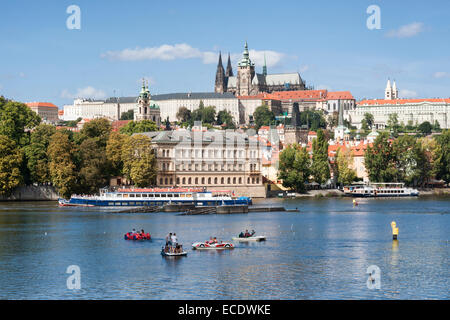 La gente in macchina a forma di barche a remi nel fiume Moldava con il quartiere del castello (Prazsky Hrad) in background, Praga, Repubblica Ceca Foto Stock