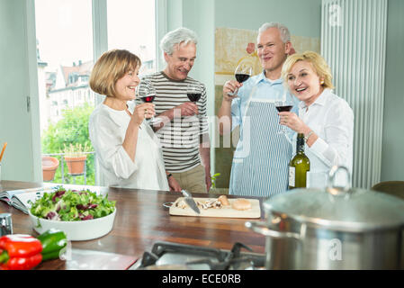 Quattro amici senior cucina cucina bere il vino Foto Stock