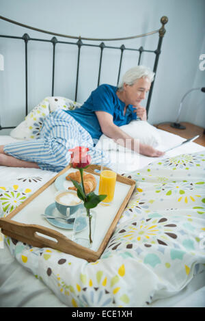 Uomo maturo avente la colazione a letto con tavoletta digitale, sorridente Foto Stock