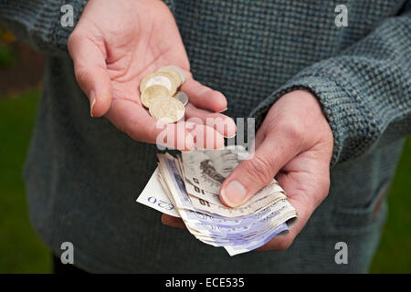 Primo piano di un uomo che tiene in mano banconote in moneta inglese banconote e monete in contanti Inghilterra Regno Unito Gran Bretagna Foto Stock