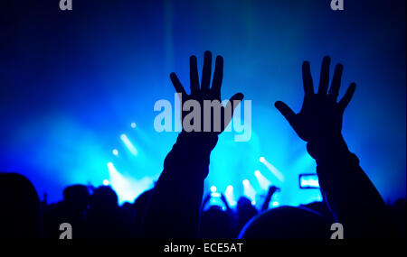 Sagome delle mani dell'uomo sollevato sopra la folla di gente, godendo di un concerto rock, luminose luci blu, per celebrare il nuovo anno Foto Stock