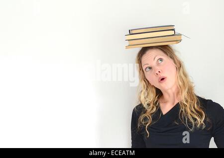 Donna che guarda fino alla pila di libri vintage equilibrato sulla testa Foto Stock