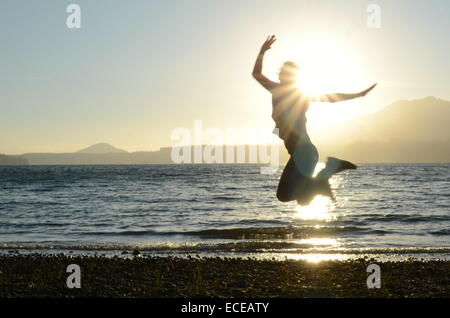 Stati Uniti d'America, nello Stato di Washington, il Parco Nazionale di Olympic, Azione girato di silhouette di donna salto sulla spiaggia al tramonto Foto Stock