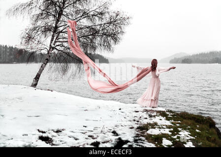 Donna con sciarpa a lungo in piedi da un lago in inverno Foto Stock