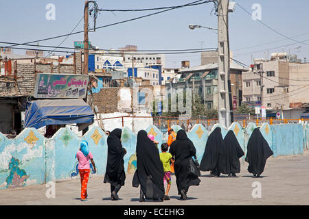 Le donne iraniane, vestito di nero burqas / burkhas, passeggiate in strada con i bambini nella città Mashhad, Razavi Khorasan, Iran Foto Stock