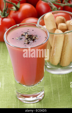 Bloody Mary cocktail con pepe macinato in un piccolo colpo di vetro, grissini e pomodoro fresco sul tavolo verde panno Foto Stock