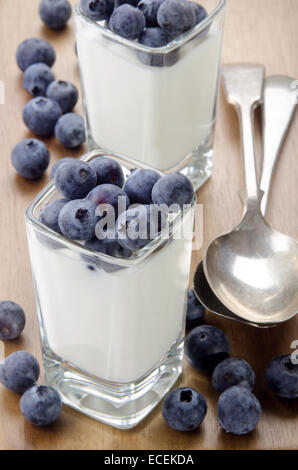 Yogurt biologici e i mirtilli in una piazza colpo di vetro e il cucchiaio sul tavolo di legno Foto Stock