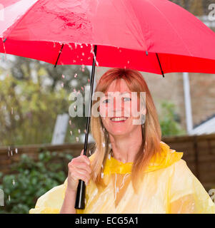 Donna che mantiene il suo red ombrello aperto durante un acquazzone pesante di pioggia Foto Stock