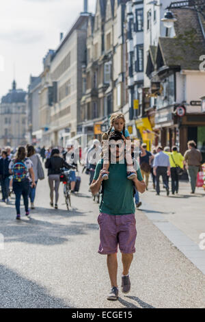 Uomo che cammina per la strada indossando occhiali da sole e corti, con sua figlia sulle sue spalle portando un orsacchiotto di peluche, Cornmarket Foto Stock