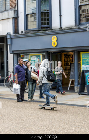 Un adolescente che indossa una giacca con cappuccio di skateboard giù Cornmarket Street, uno di Oxford le principali vie dello shopping. Foto Stock