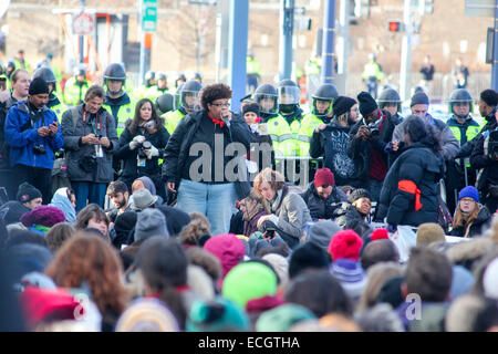 Boston, Massachusetts, USA. 13 dicembre, 2014. Un manifestante parla mentre altri sedersi e guardare la polizia in background durante i milioni marzo rally a Boston, Massachusetts, USA. La protesta, simili a quelli di altre città in tutto il territorio degli Stati Uniti in questo giorno, è in risposta ai recenti grand jury verdetti non incriminante i poliziotti che hanno ucciso disarmato gli uomini neri Michael Brown e Eric Garner, e per le persistenti problemi del razzismo e della polizia brutalità. Credito: Susan Pease/Alamy Live News Foto Stock