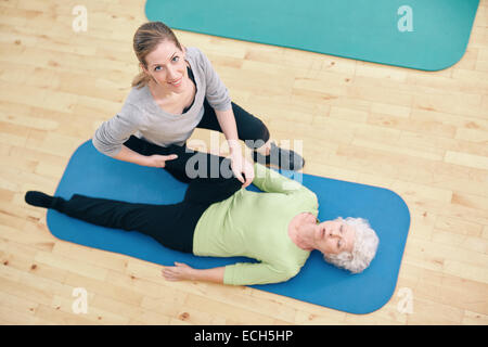 Vista dall'alto del fisioterapista che aiuta la donna anziana a fare strette alle gambe presso il centro di salute. allenatore di palestra che assiste una donna anziana nella gamba Foto Stock