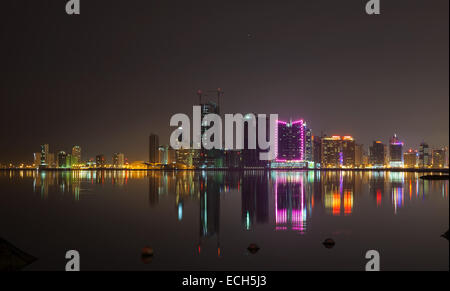 Notte moderno skyline della città con brillanti luci e riflessi nell'acqua. Manama, la capitale del Regno del Bahrain, Medio Oriente Foto Stock