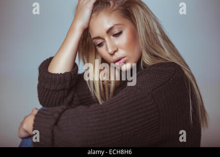 Contemplativo giovane donna in maglia. Piuttosto giovane donna che guarda verso il basso nel pensiero. Foto Stock