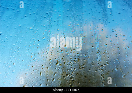 Close up di goccioline di acqua sul vetro della finestra, colori vivaci dal cielo e gli alberi al di fuori del display attraverso l'acqua. Foto Stock