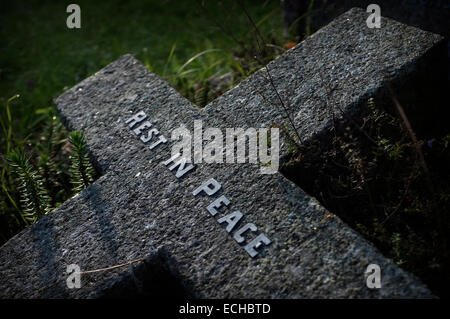 Una testa a croce posa della prima pietra in un cimitero, il lato illuminato con luce solare evidenziando le parole riposi in pace. Foto Stock