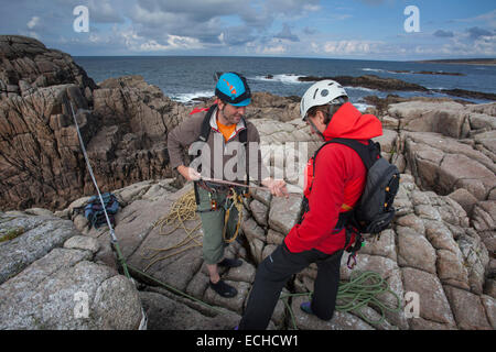 Arrampicatori preparando le corde per una traversata tirolese per accedere a una pila di mare. Gweedore, County Donegal, Irlanda. Foto Stock