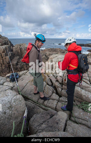 Arrampicatori preparando le corde per una traversata tirolese per accedere a una pila di mare. Gweedore, County Donegal, Irlanda. Foto Stock