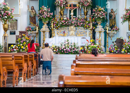 Popolo messicano pregando in una chiesa a Puerto Vallarta, Messico. Un uomo si avvicina l altare e dire una preghiera sulle sue ginocchia. Foto Stock