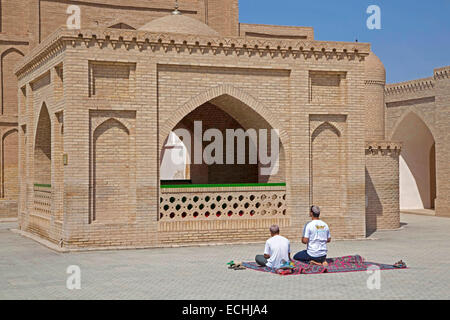 Due turkmeni pregando sul tappetino nella parte anteriore del Mausoleo di Hoja Yusuf Hamadani nella città di Merv / Merw vicino a Maria, Turkmenistan Foto Stock