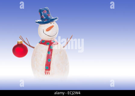 Pupazzo di neve decorativo tenendo un ornamento di Natale. Blu e sfondo bianco con copia spazio. Foto Stock