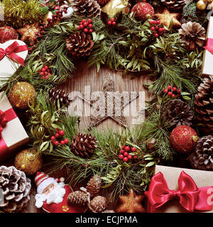 Un rustico tavolo in legno pieno di regali e decorazioni di Natale, come una ghirlanda di naturale con rami, bacche e pigne, o Foto Stock