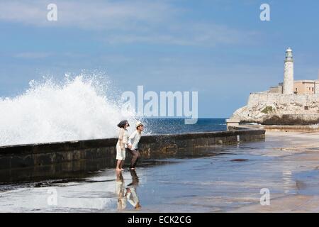 Cuba, La Habana, onda oltre il Malecon, turisti e Castillo de los Tres Reyes Magos del Moro in background Foto Stock