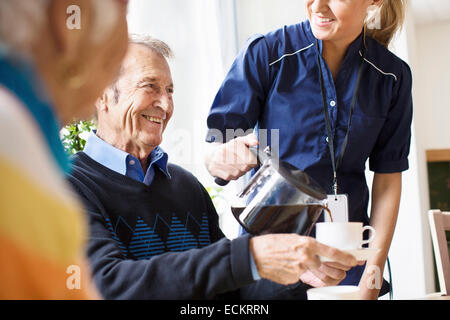 Sezione mediana di felice custode femmina che serve caffè nero per uomo senior presso la casa di cura Foto Stock