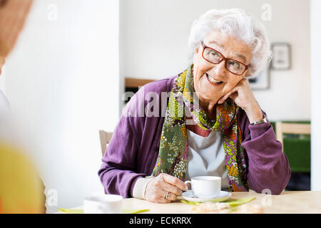 Felice senior donna guardando amico pur avendo caffè al tavolo per la colazione nella casa di cura Foto Stock