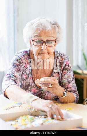 Senior donna assemblaggio di pezzi di puzzle a tavola in casa di cura Foto Stock