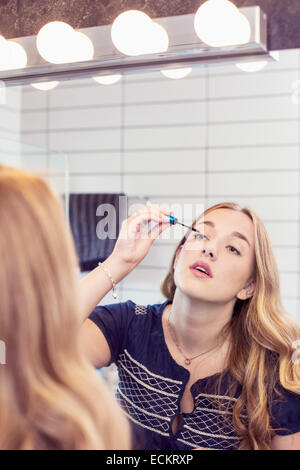 Giovane donna applicazione di mascara di fronte a Specchio bagno Foto Stock