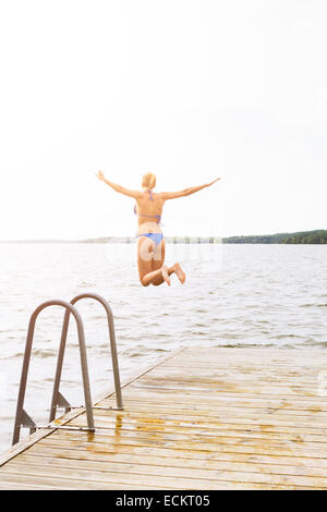 Vista posteriore della donna con le braccia aperte saltando nel lago Foto Stock