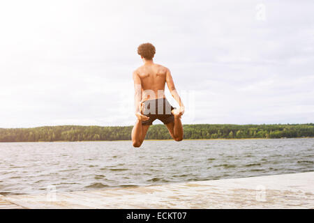 Lunghezza piena vista posteriore dell'uomo tenendo le gambe durante il salto nel lago Foto Stock