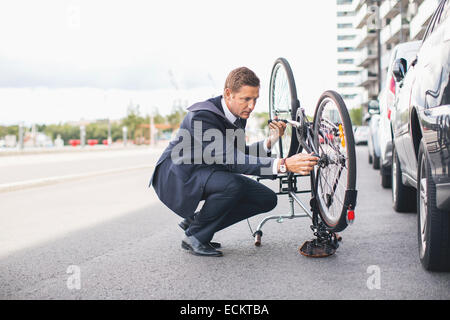 Imprenditore il fissaggio della catena di una bicicletta su una strada di città contro sky Foto Stock