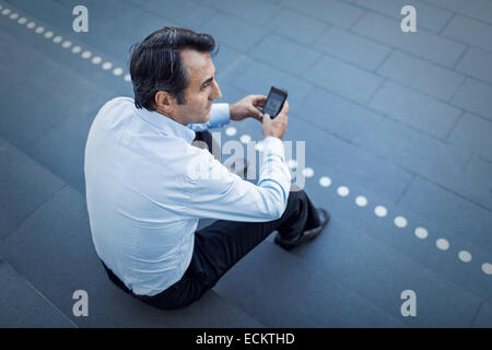 Elevato angolo di visione dell'uomo d'affari alla ricerca di distanza mentre si utilizza il telefono cellulare su gradini Foto Stock