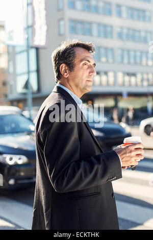 Vista laterale di imprenditore che guarda lontano tenendo monouso tazza di caffè in città Foto Stock