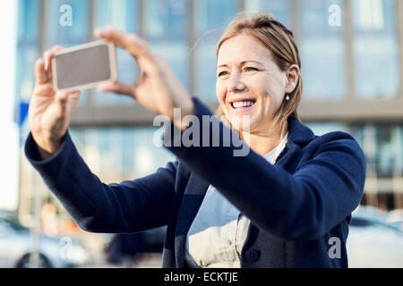 Felice imprenditrice fotografare con smart phone all'aperto Foto Stock