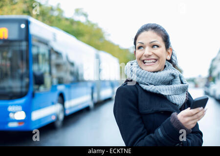 Sorridente metà donna adulta parlando su smart phone su strada Foto Stock