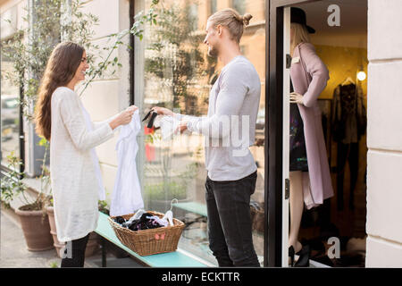 Felice proprietario di sesso maschile che mostra prezzo di etichetta della calzatura al cliente esterno boutique Foto Stock