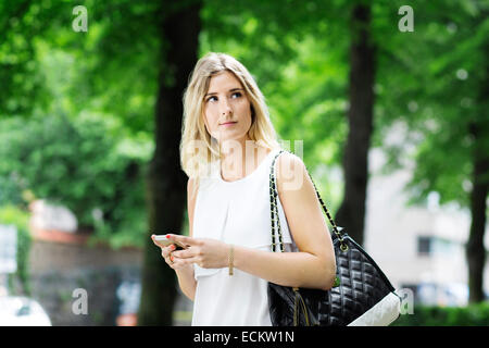 Giovane donna tenendo il telefono cellulare mentre cerchi di distanza all'aperto Foto Stock