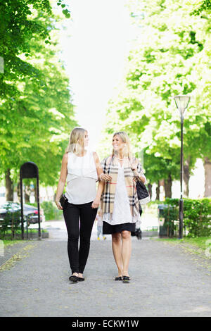 Lunghezza completa di felice amiche comunicante camminando sul percorso del giardino Foto Stock