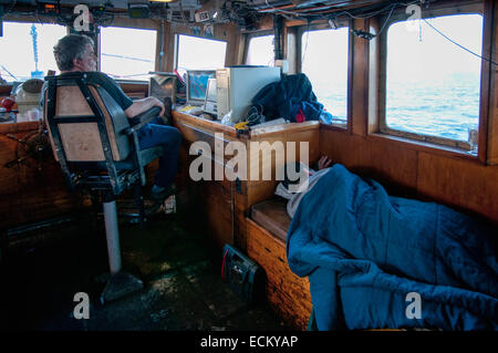 Il capitano tiene guarda su dati elettronici in cabina di pesca mentre dragger crewman pan. Foto Stock