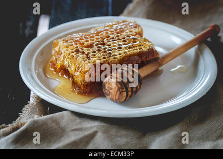 Favo di miele bilanciere su piastra in ceramica su un vecchio tavolo di legno. Foto Stock