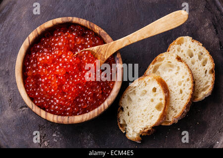 Caviale rosso in legno d'olivo ciotola e pezzi di pane su sfondo scuro Foto Stock