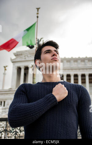 Orgoglioso giovane uomo nella parte anteriore della bandiera italiana con fiduciosa espressione in Roma con il Vittoriano dietro di lui Foto Stock