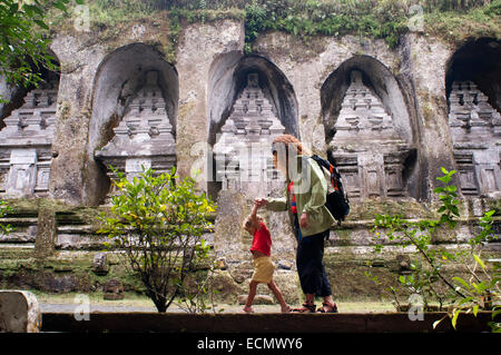 Un turista con un bambino guarda i grandi santuari scavati nella rupe-faccia presso il Gunung Kawi templi. Tirtha Empul Tempio è Foto Stock