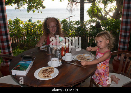 Una madre avente la prima colazione con la figlia in un ristorante di Amed. Bali. Indonesia. Viaggiare con chindren. Amed si riferisce a un lungo tratto di costa che da il villaggio di Cucik circa 14 km a est che incorporano i sette villaggi di Amed, Jemeluk, Bunutan, Lipah, Selang, Banyuning e AAS. Il ritmo della vita è lento e il paesaggio costiero abbastanza stupefacente rendendo Amed il luogo perfetto per trascorrere una rilassante vacanza in Bali. Foto Stock