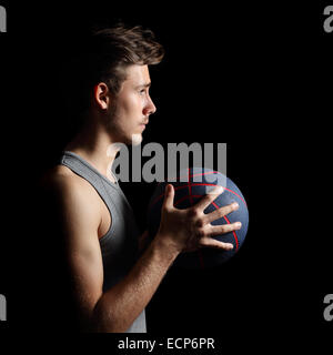 Vista laterale di un giocatore di basket tenendo un canestro isolato su sfondo nero Foto Stock