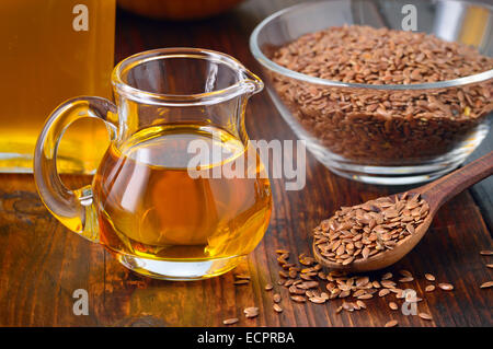 Brown semi di lino sul cucchiaio e olio di lino in caraffa di vetro su un tavolo di legno. Olio di lino è ricco in acido grasso omega-3. Foto Stock