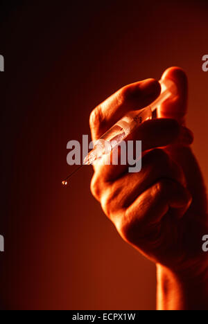 Minacciando la mano con la siringa nel sangue-luce rossa. Foto Stock